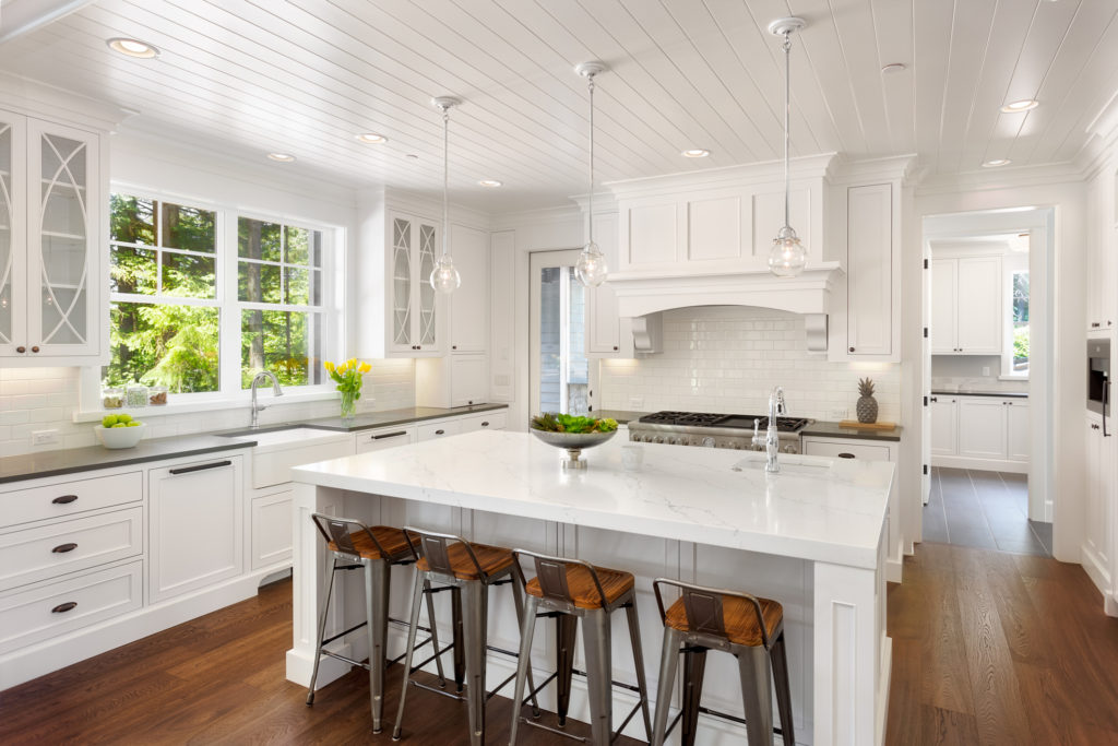 White Kitchen Interior with Island, Sink, Cabinets, and Hardwood Floors in New Luxury Home with Lights On