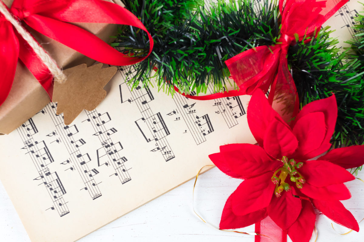 Christmas ornament and music sheet on white natural wooden table. Red ribbon bow. Poinsettia. Gift or present with label and twine.