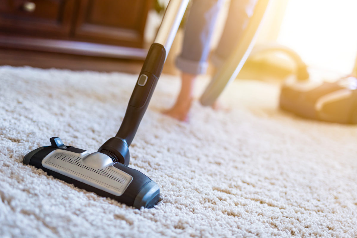 Young woman using a vacuum cleaner while cleaning carpet in the house.