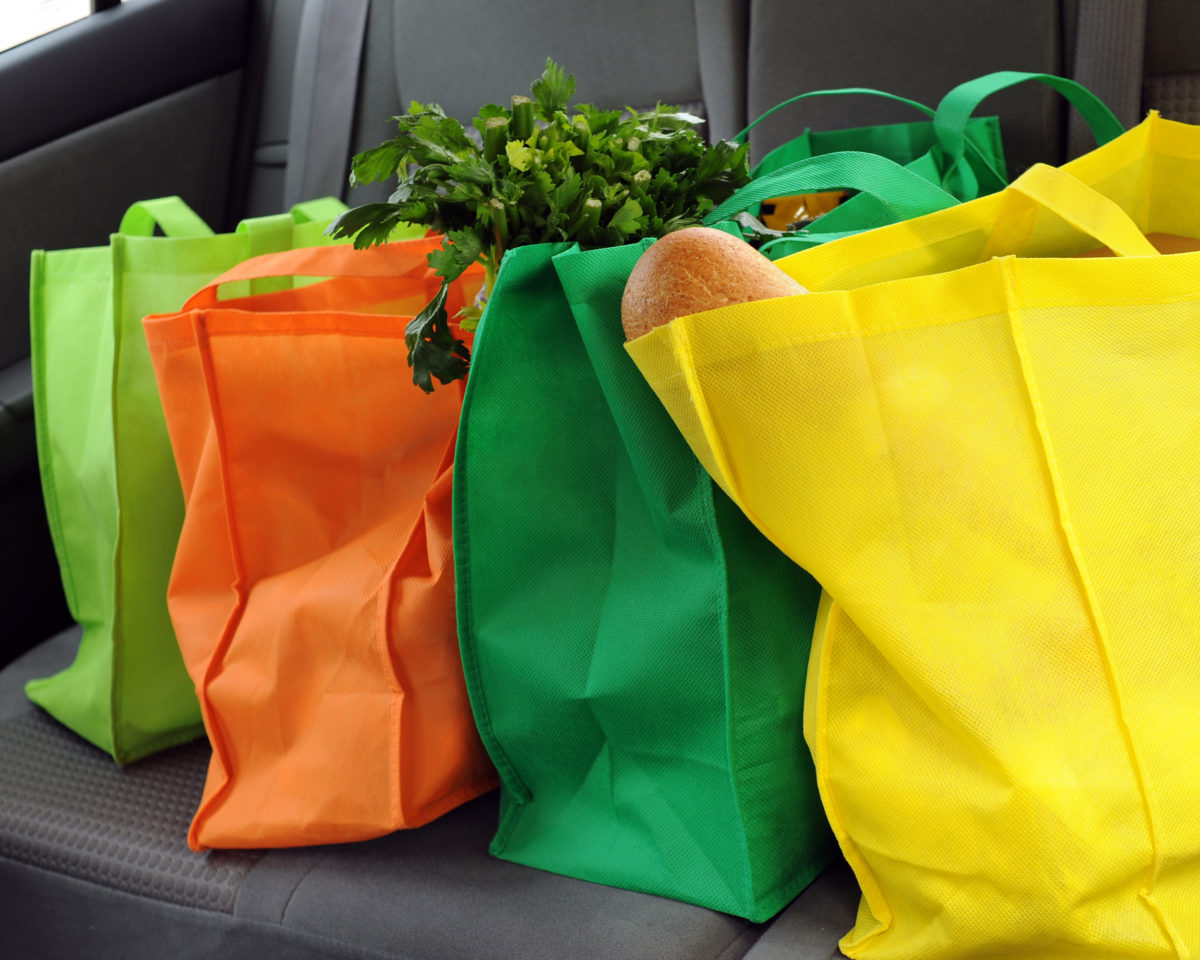 Four filled and colorful eco-friendly shopping bags in the back seat of a car.