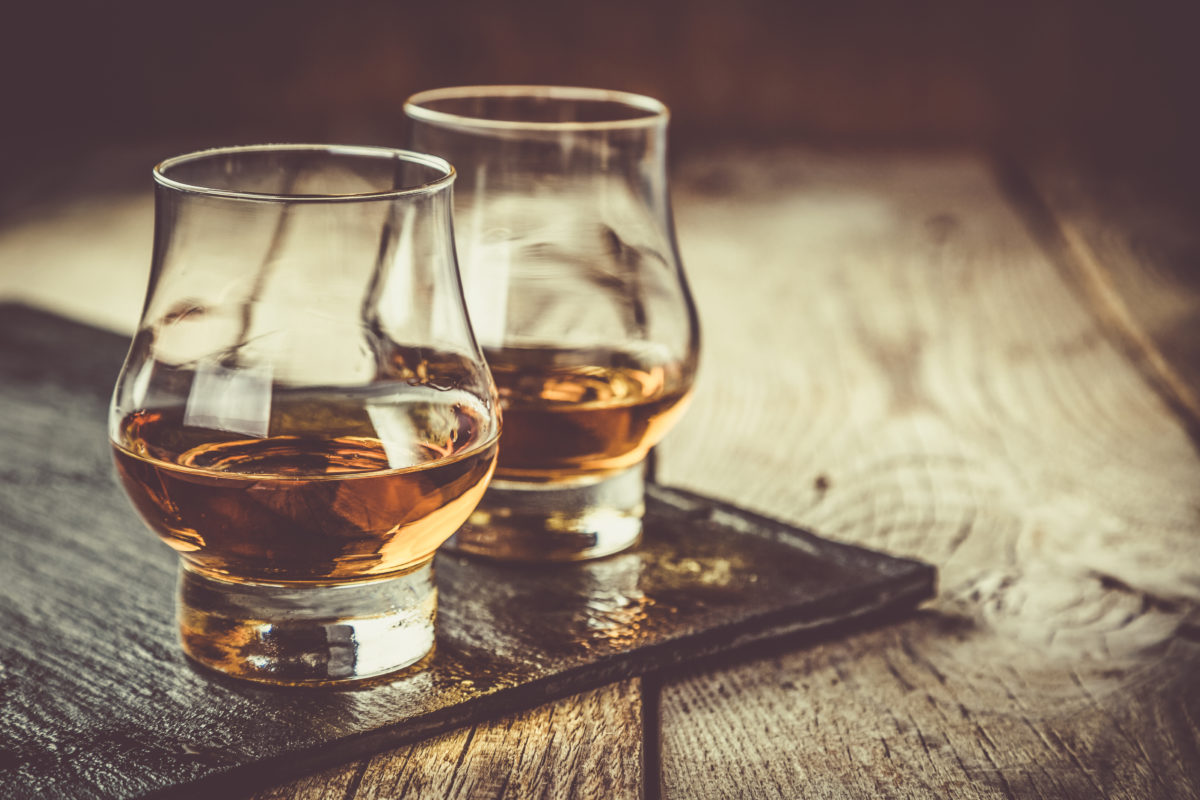 Whiskey with ice in glasses, rustic wood background, copy space