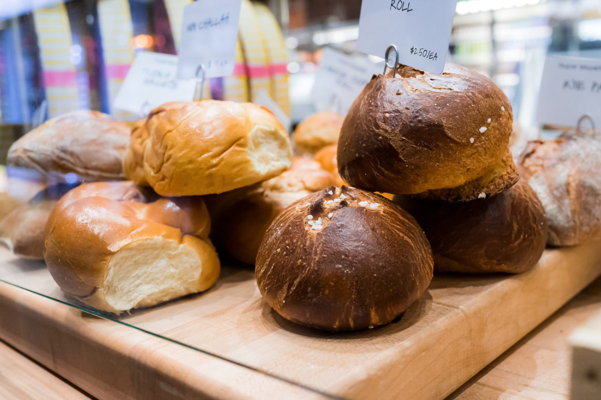 Closeup of fresh brown whole wheat dark sourdough baked bread loaves rolls in bakery with many buns, challah