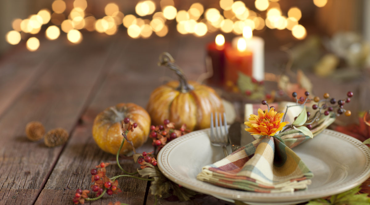 Autumn Thanksgiving dining table place setting on an old rustic wood table with candles and defocused Christmas lights