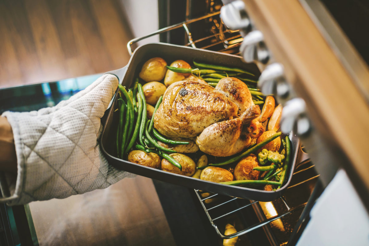 Cook taking ready fried baked chicken with vegetables from the oven. Healthy cooking concept.