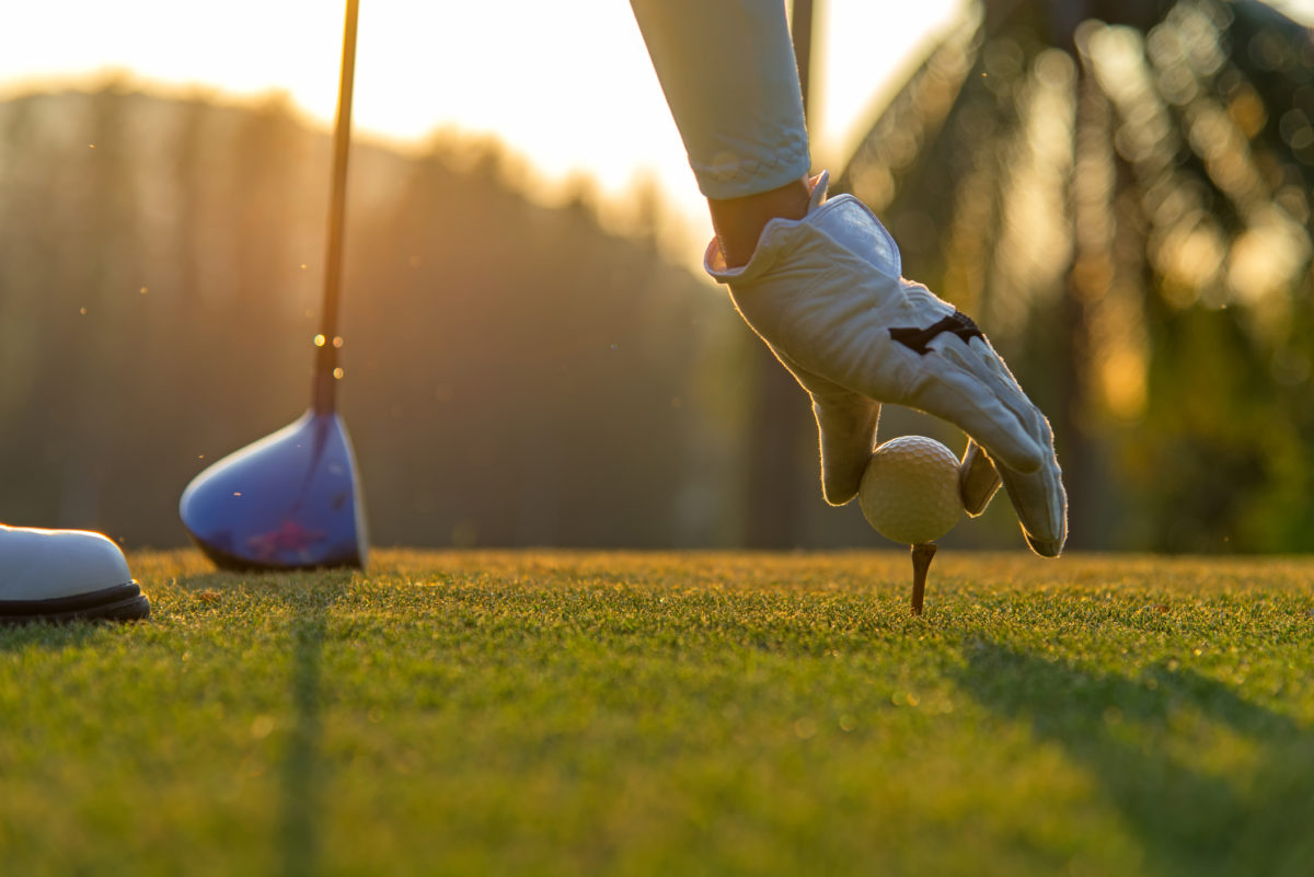 Hand asian woman putting golf ball on tee with club in golf course on evening and sunset time a for healthy sport. Lifestyle Concept