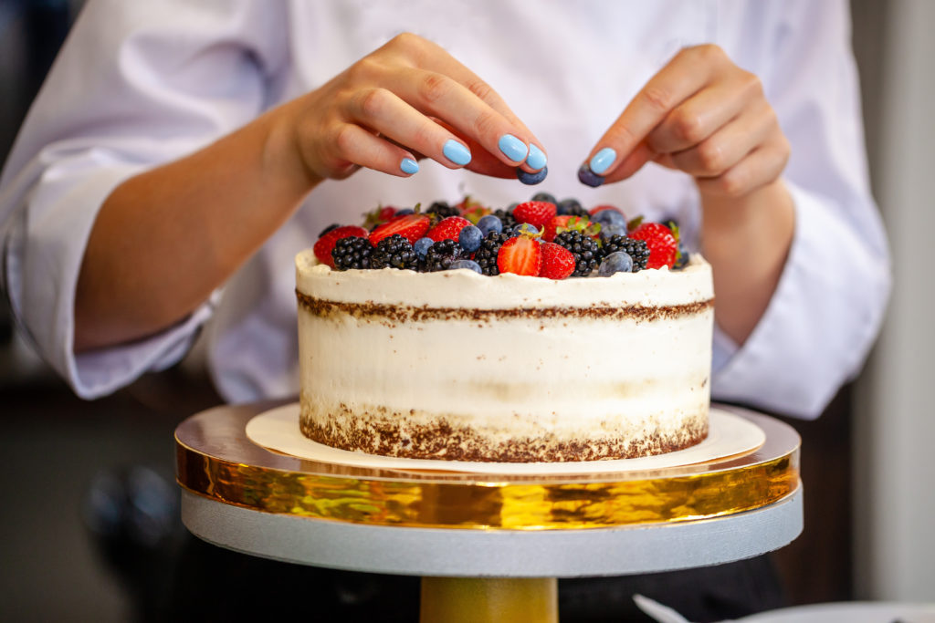 Girl chef cooks confectioner, decorates cake with forest berries. concept making without lactose cakes. Copy space, selective focus