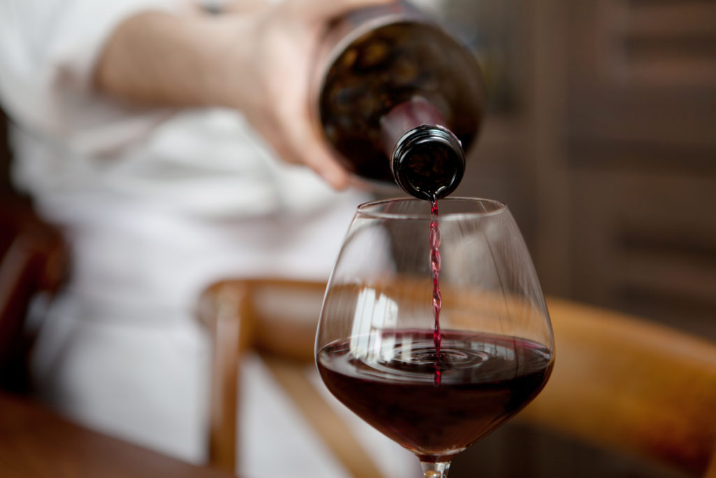 Waiter pours red wine into a wine glass