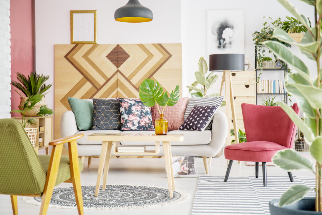 Patterned pillows on sofa next to red armchair in cozy living room interior with wooden furniture