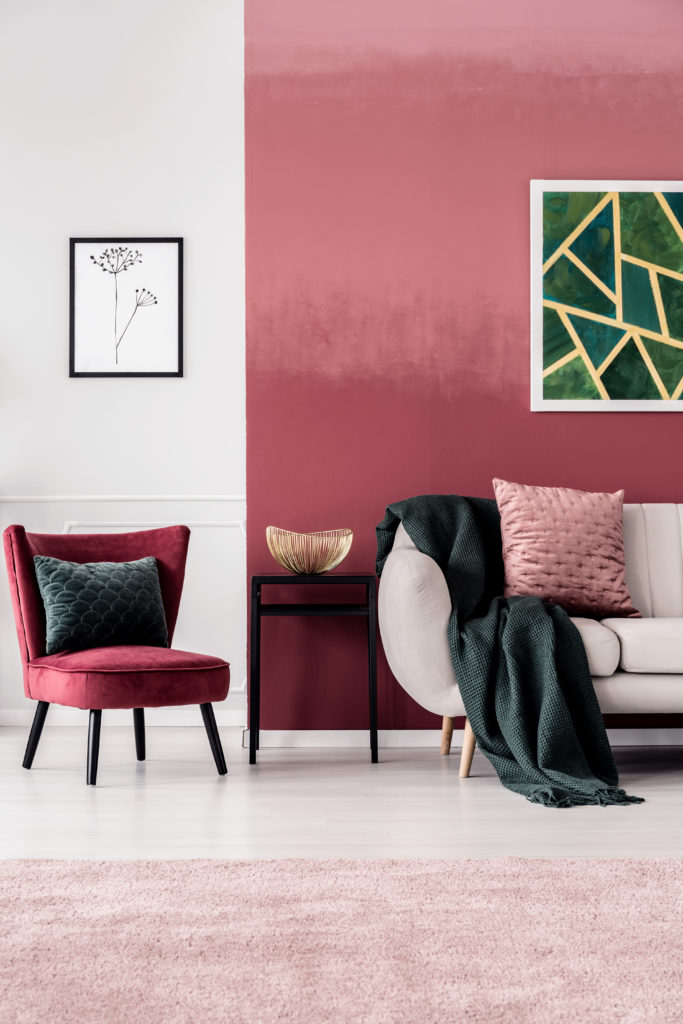 Feminine living room interior with burgundy armchair and dark green blanket on a beige sofa standing against an ombre wall